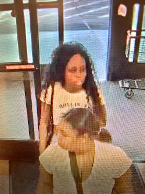 Photo of third female suspect wearing a white Holister crop-top, shorts and sandals. Suspect has long curly black hair.